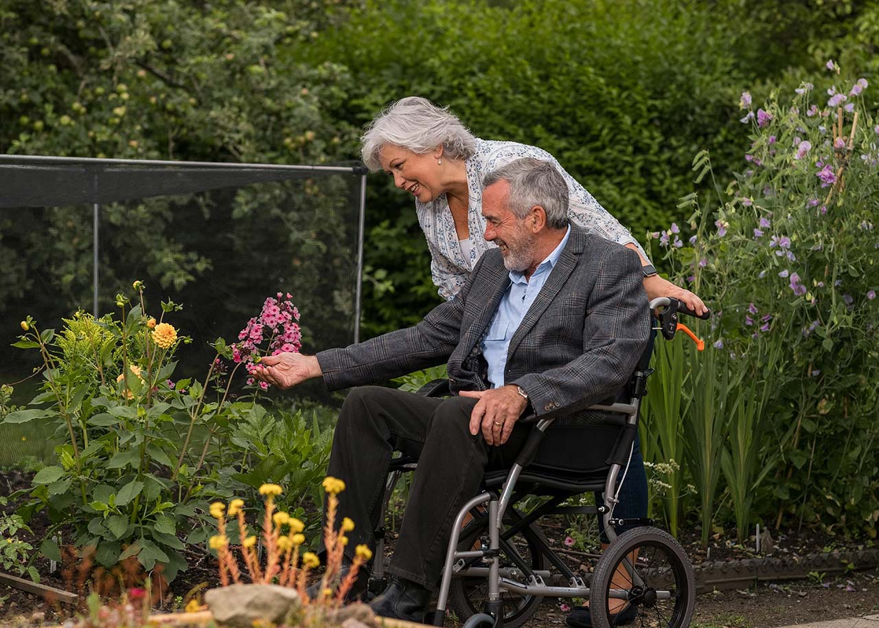 A happy elderly couple of a man in a wheelchair and a woman in a garden.