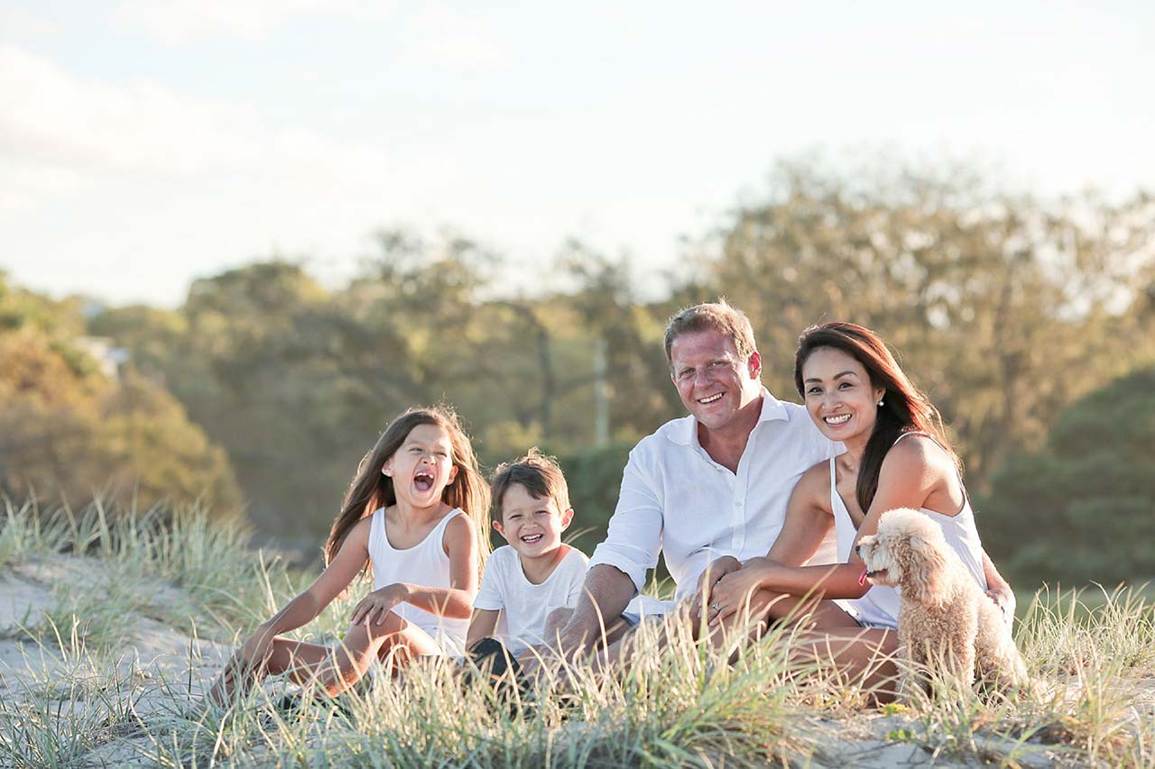 A family of a man, woman, young boy and young girl sitting in grass.